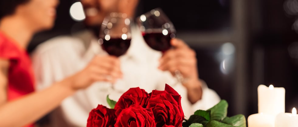 Couple enjoying red wine with a bouquet of roses in front fo them
