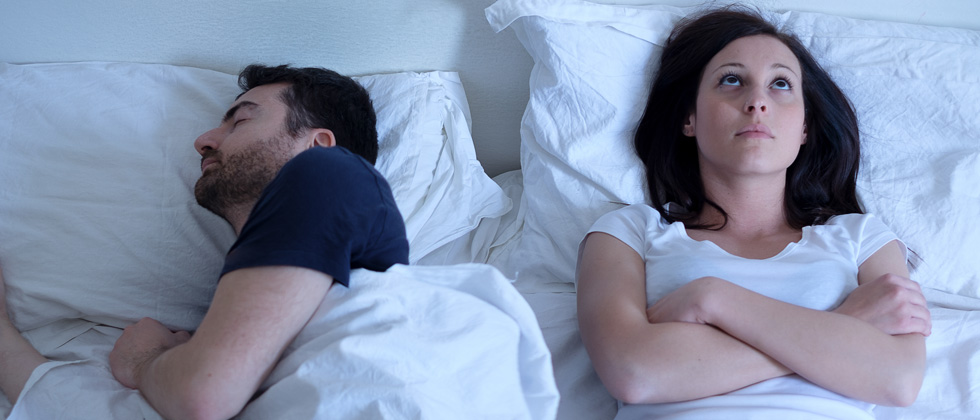 Man sleeping peacefully next to a woman who is awake thinking