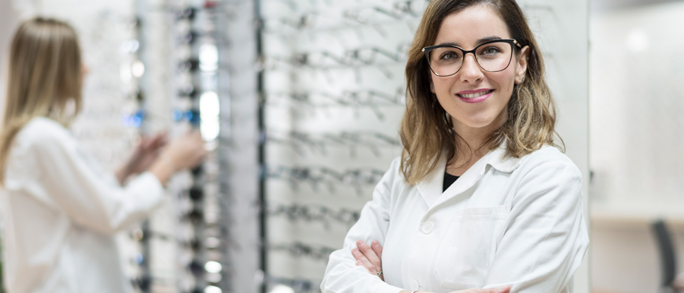 A female eye doctor standing next to a wall of sample glasses
