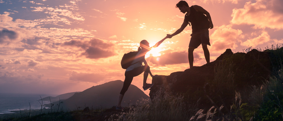 Couple on a hike & one is helping the other up a big step