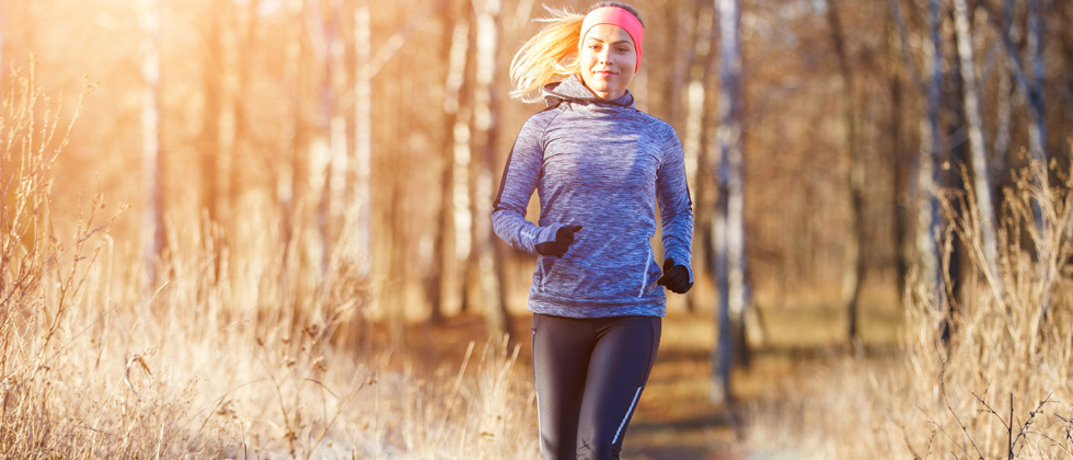 A female runner jogging on a wooded path in the sun