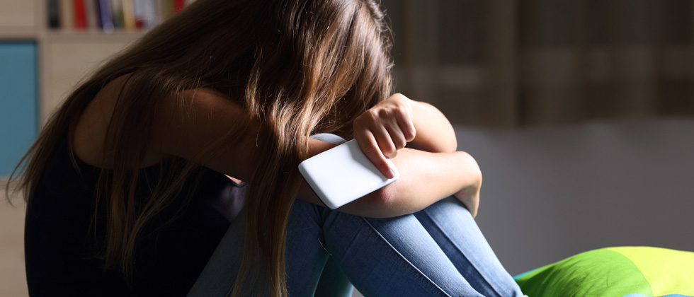 A woman upset crying into her arms while holding her phone