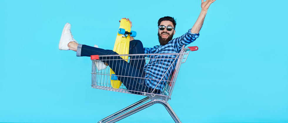A guy sitting in a shopping cart with a skateboard