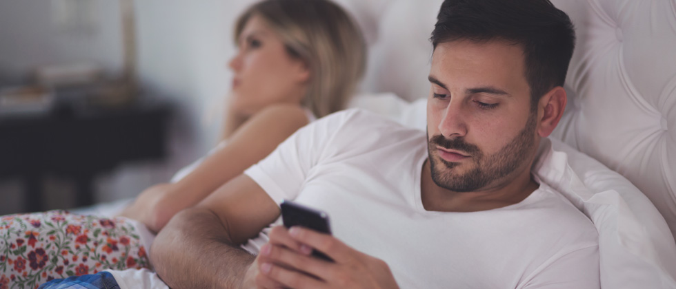 A couple in an argument in bed while the guy texts