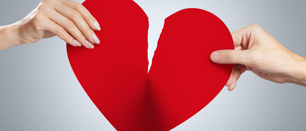 A big paper heart being riped by two people pulling at it