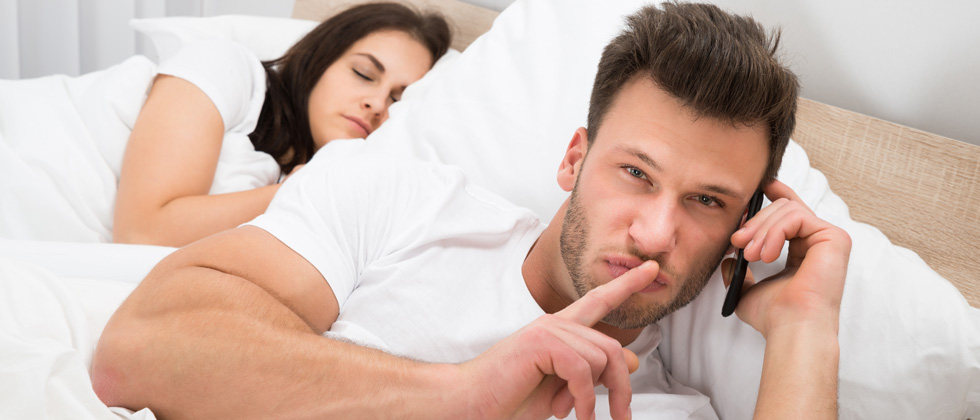 A couple sitting in bed - one sleeping the other one is secretly the phone