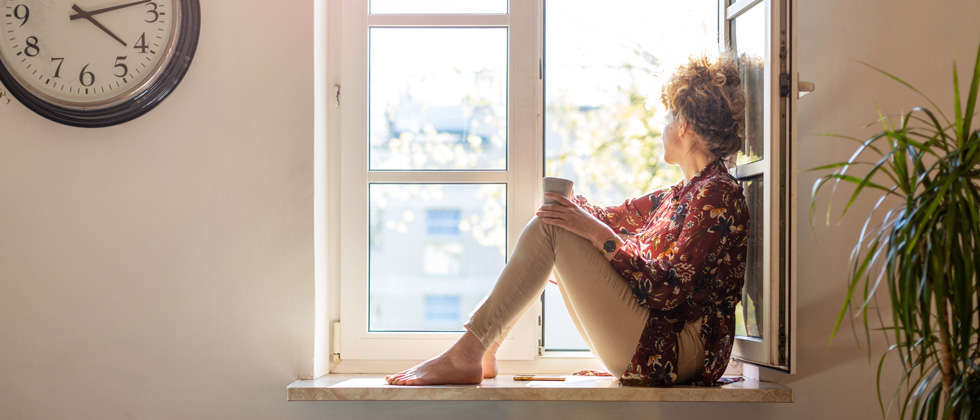 A woman sipping coffee sitting on her windowsill looking out