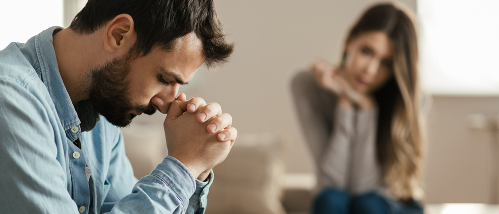 A man looking angry with a woman looking upset in the background