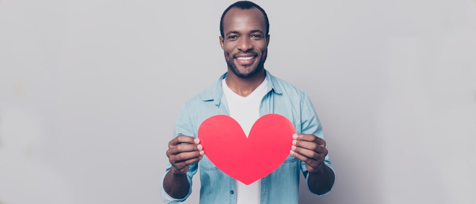 A man standing holding up a cutout heart & smiling