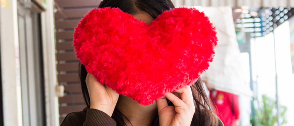 Someone covering their face with a big red heart-shaped pillow