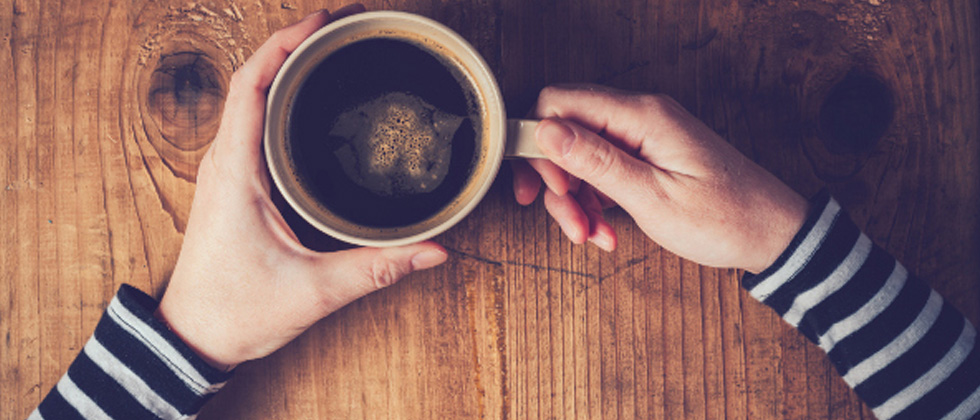 Someone sitting alone holding a black cup of coffee