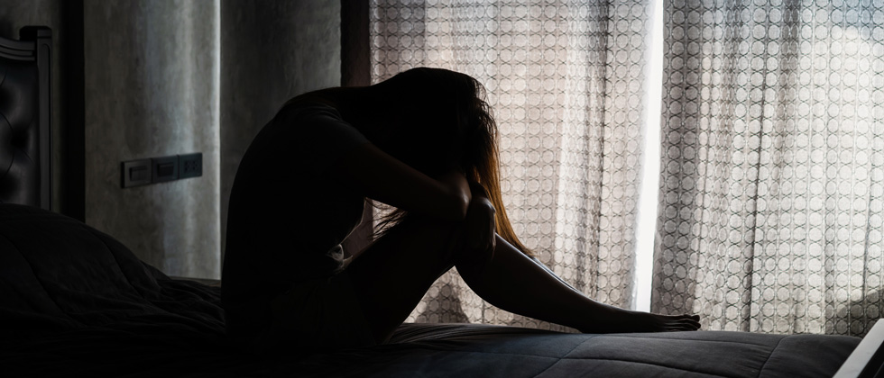 A woman curled up in the dark crying into her arms