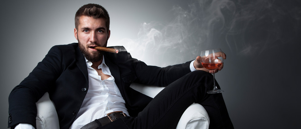 Attractive man lounged on a chair smoking a cigar and drinking wine