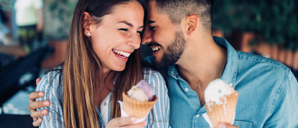 A cute couple flirting while eating ice cream cones together