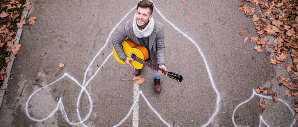 Guy standing in a chalk drawn heart playing the guitar