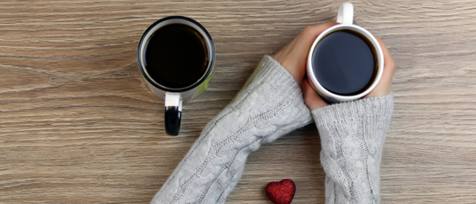 Someone sitting holding a cup of coffee with a second one next to them