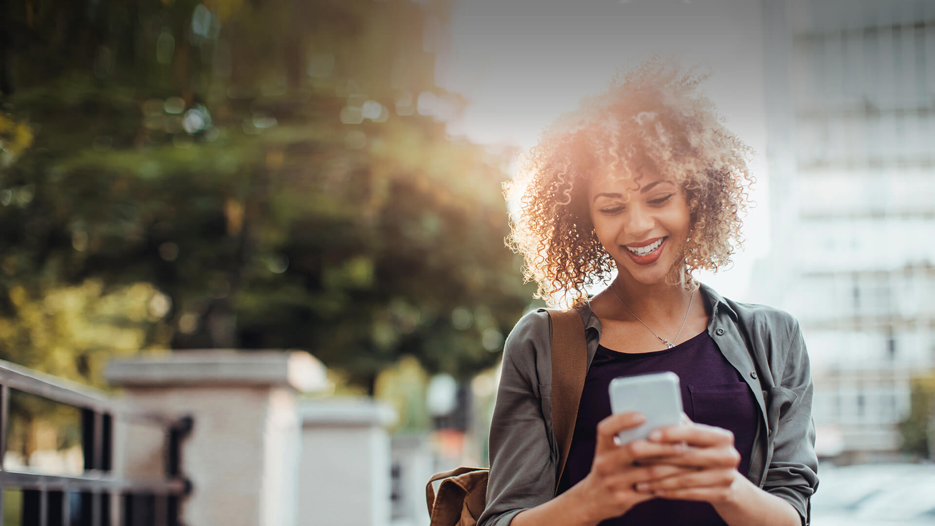 Black single woman smiles in her smartphone while dating online on the go in Canada