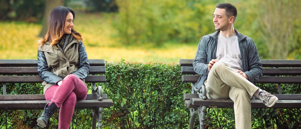 A man & woman sitting on separate park benches chatting