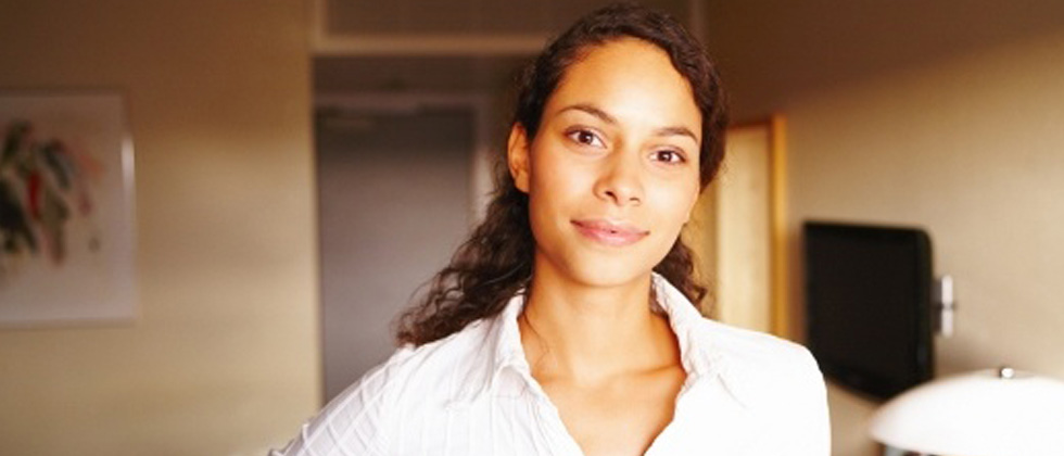 A woman standing in her apartment slightly smiling into the camera