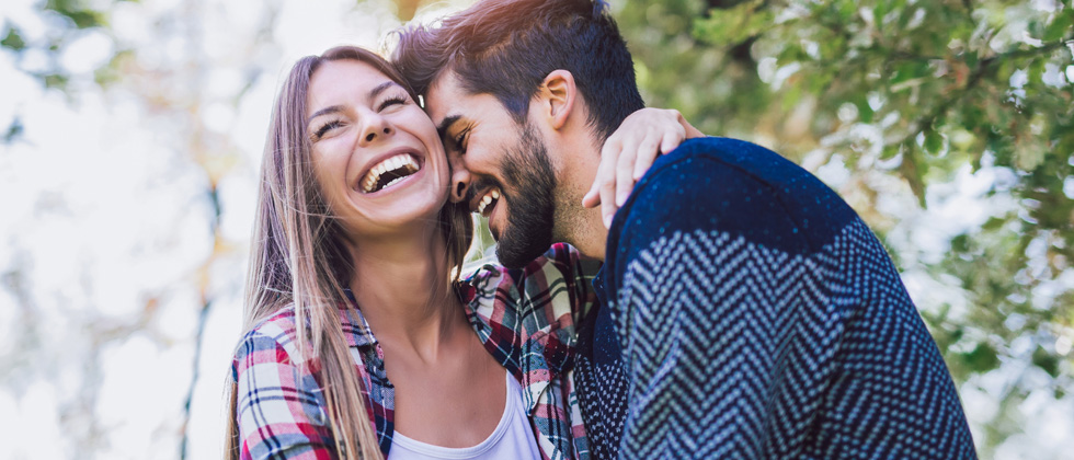 Happy couple cuddling and laughing in the sunlight