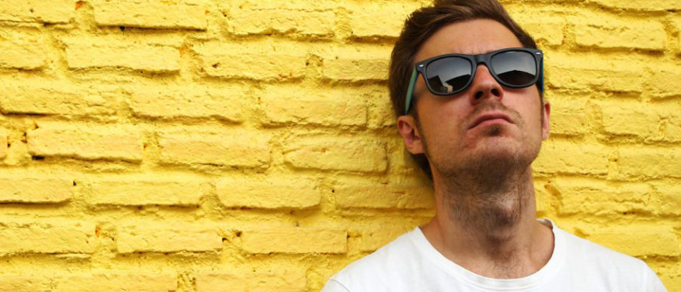 Young man leaning against a brick wall looking unapproachable