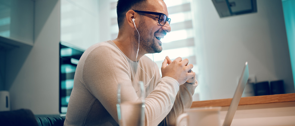 Man on his computer with headphones laughing