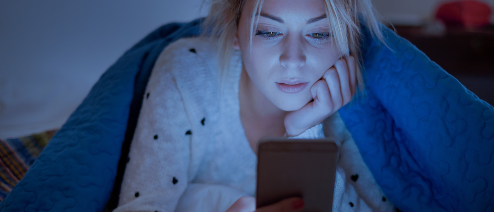 Woman lying in bed on her phone late at night