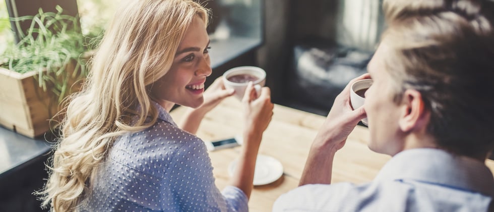 Beautiful smiling girl drinking coffee talking to a young man