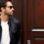 A guy in a leather jacket and sunglasses looking away as he walks