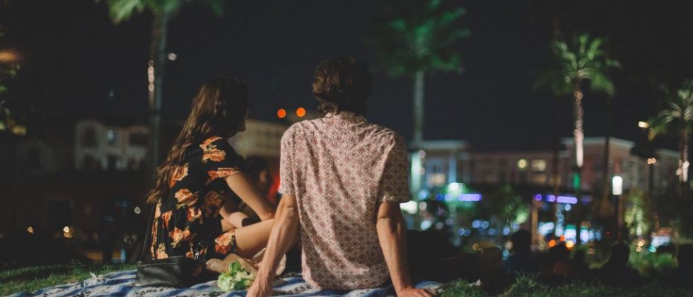A young couple sitting on a picnic blanket in the park at night