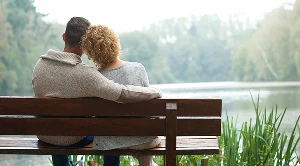A couple enjoying a peacful moment together on a bench next to a lake.