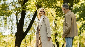 A couple together on a park walk date next to green trees.