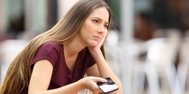 Woman with cell phone in hand looks thoughtful and considers how to cancel a date