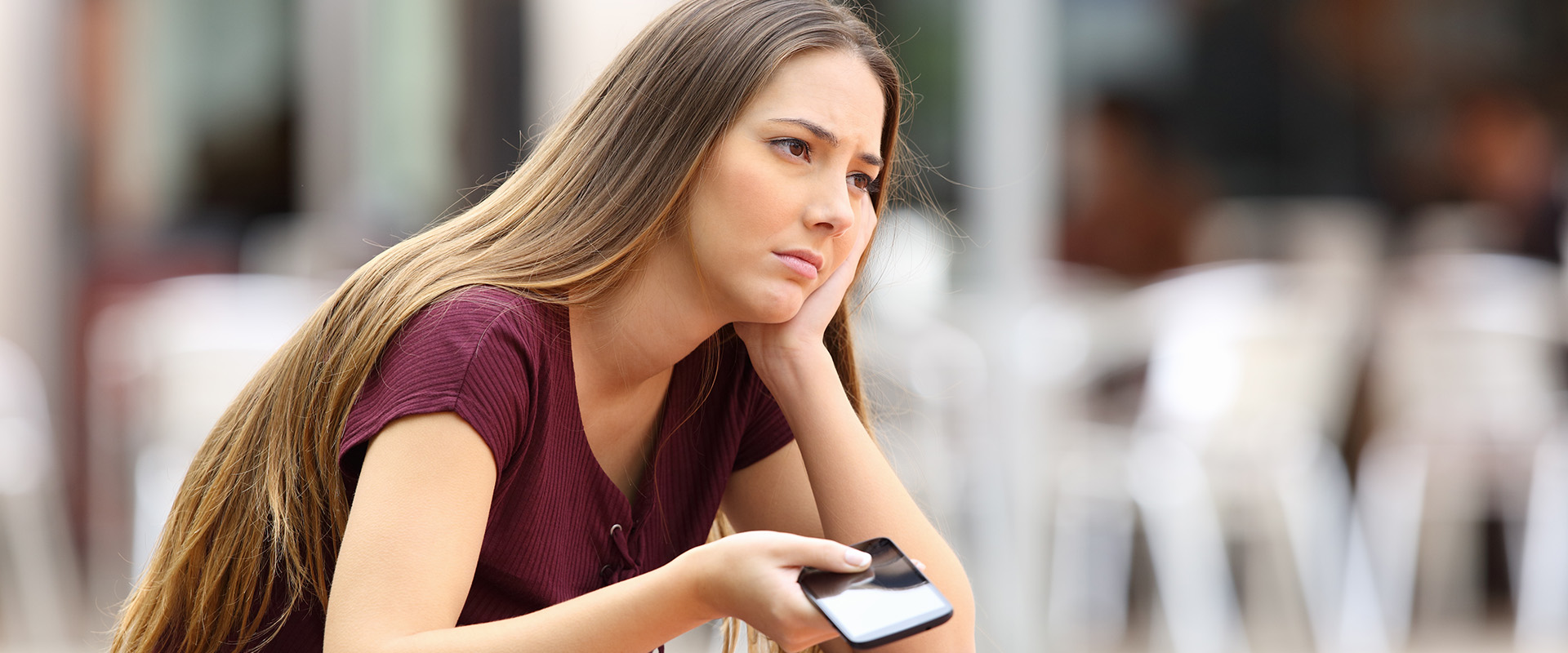 Woman with cell phone in hand looks thoughtful and considers how to cancel a date