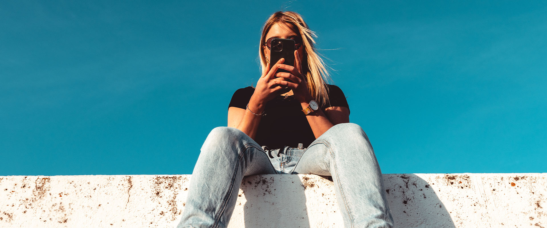 Woman sitting on wall with cell phone in hand as symbol for online dating safety