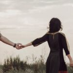 Couple in a field holding hands but walking away from each other