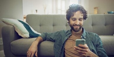 Man with cell phone in hand on the sofa informs himself about tips for eharmony settings