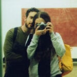 A man and a woman standing next to each other, photographing themselves in the mirror.