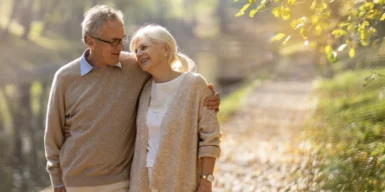 A couple walk side by side along a gravel path near a forest in the sunlight.