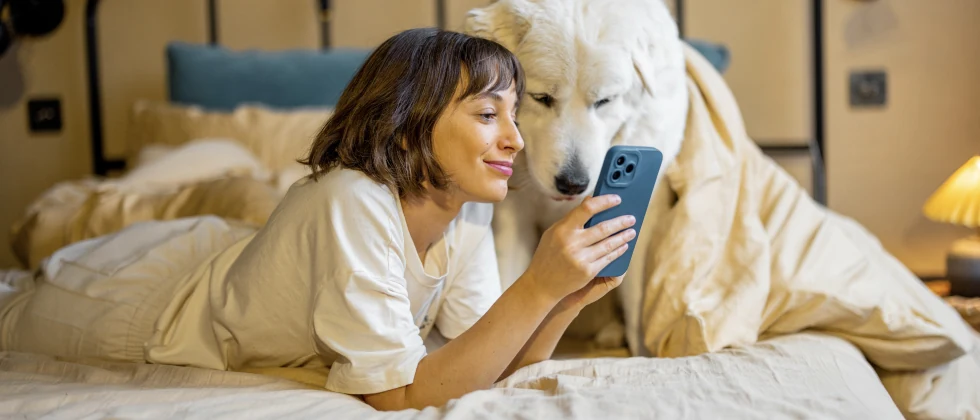 Woman sitting with her dog on the bed and looking to her phone.