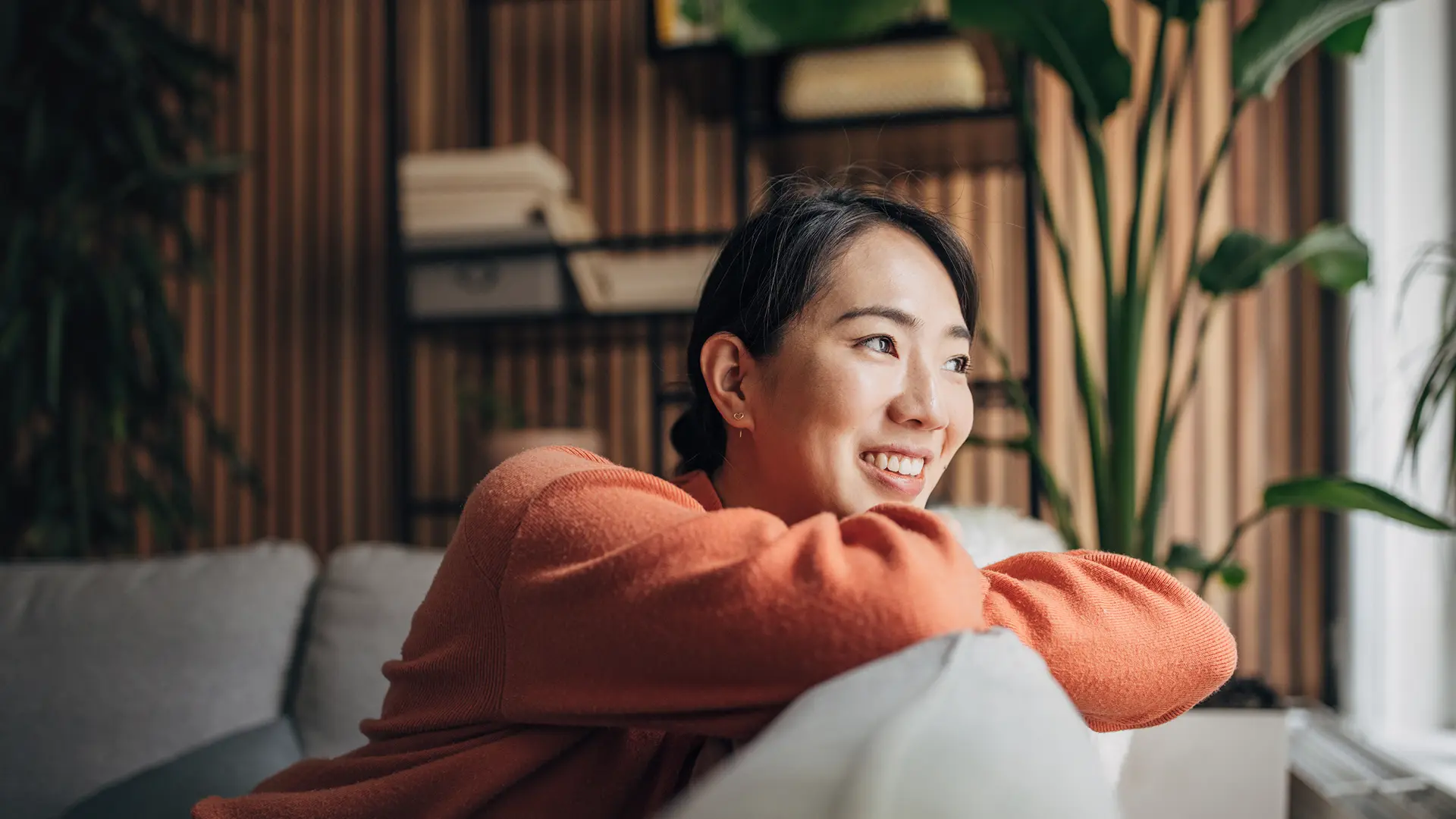 Asian Women on the couch in her living room looking out of the window.